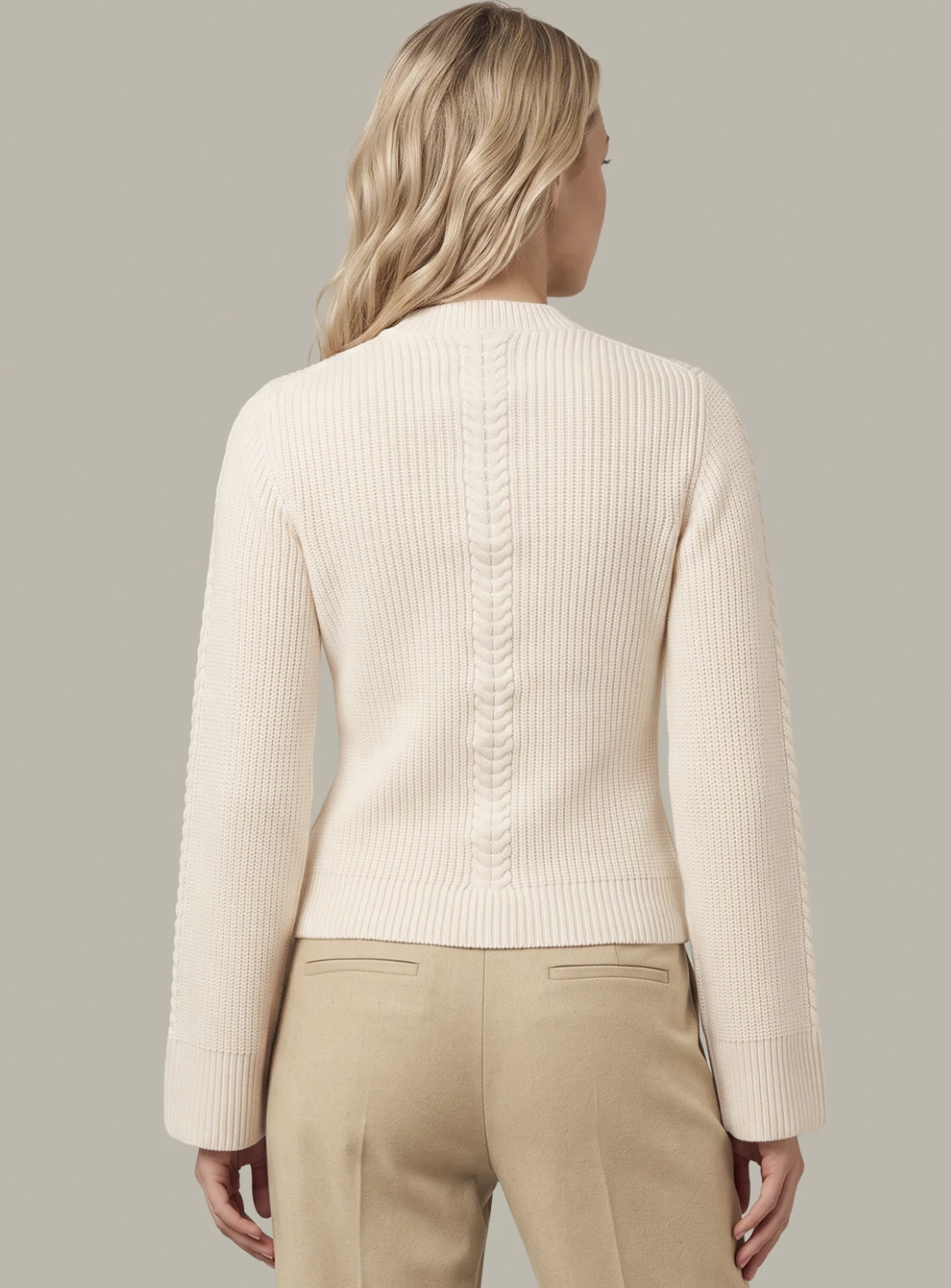 A woman shown from the back wearing a cream ribbed knit 525 America cardigan with textured sleeve panels and beige trousers, against a solid light gray background.