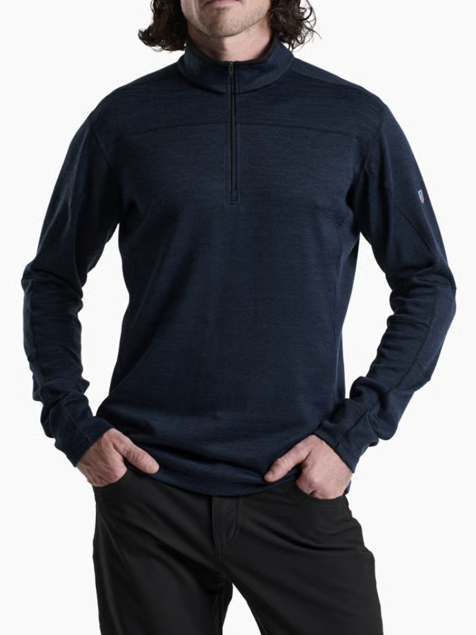 A man wearing a Kuhl Ryzer dark navy blue quarter-zip long-sleeve performance pullover with black pants, shown from the chin down against a plain white background.