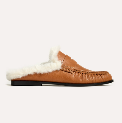 A Yosi Samra Camden tan leather slip-on loafer with a plush white shearling lining, shown in a side profile on a light off-white background.