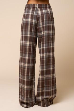 A pair of wide-leg plaid trousers in brown, beige, and gray, shown on a model from the waist down against a solid beige background.