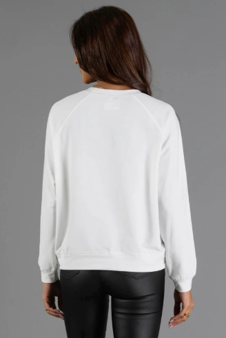A woman viewed from the back wearing a plain white long-sleeve crewneck sweatshirt and black pants, standing against a solid gray studio background.
