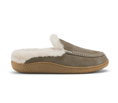 A single Olukai Nohea Kolo slip-on mule slipper shown in profile against a white background. The slipper has a taupe-brown suede upper, a fluffy white shearling lining, and a tan rubber sole.
