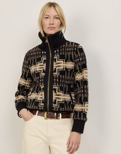 A woman modeling a black and beige patterned Pendleton zip-up jacket with a high collar, paired with cream pants and a brown belt, against a plain light gray background.