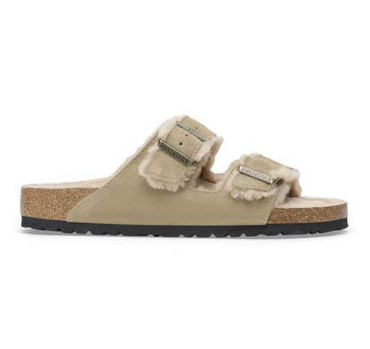 A pair of Birkenstock Arizona Shearling slip-on sandals in beige faux leather with fluffy cream shearling lining, cork midsoles, and black outsoles, shown from a side profile on a white background.