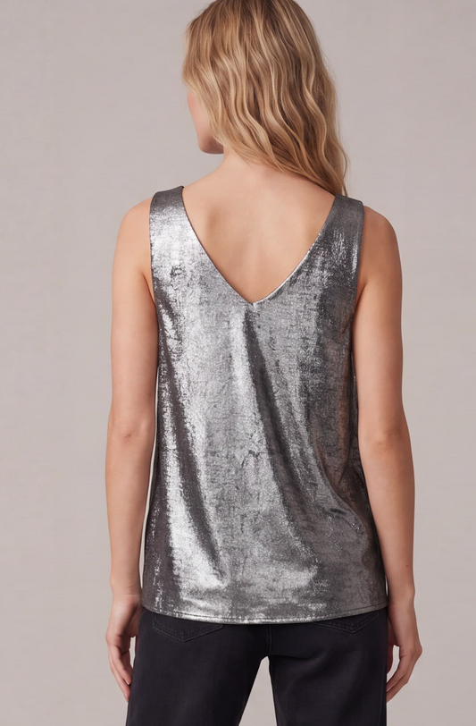 A woman viewed from the back wearing a sleeveless metallic silver tank top with a deep V-neck and dark pants, set against a plain light gray studio background.