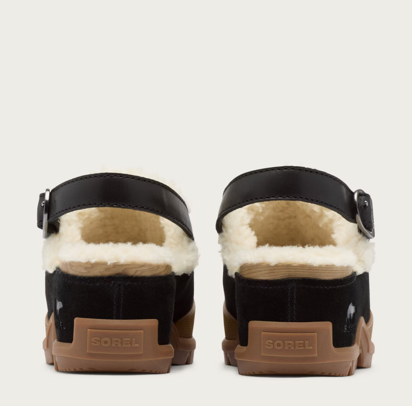 A pair of Sorel clogs shown from the back, featuring black suede and faux-leather uppers with a thick white shearling lining, brown rubber soles, and the Sorel brand name embossed on the heel.