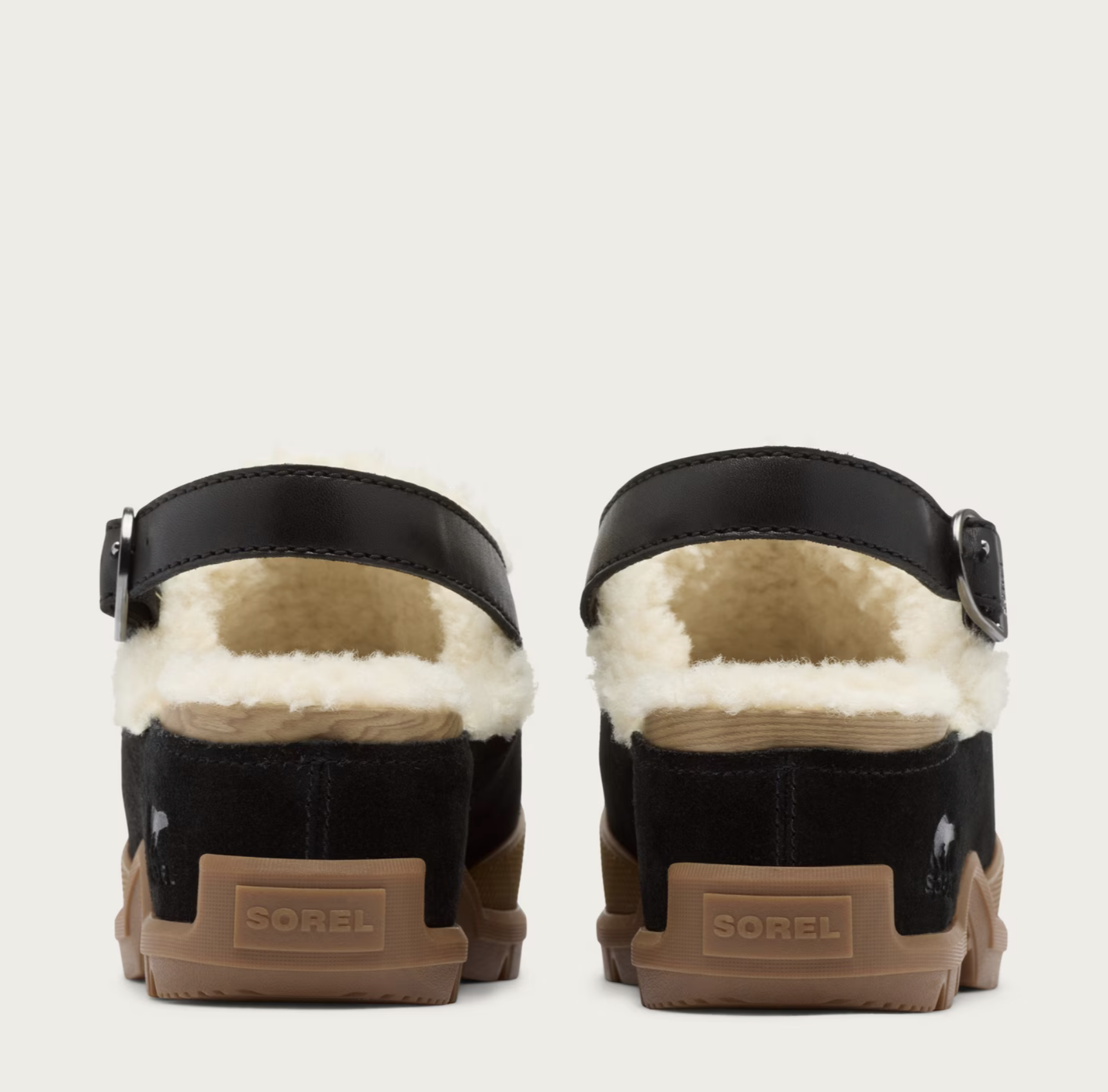 A pair of Sorel clogs shown from the back, featuring black suede and faux-leather uppers with a thick white shearling lining, brown rubber soles, and the Sorel brand name embossed on the heel.