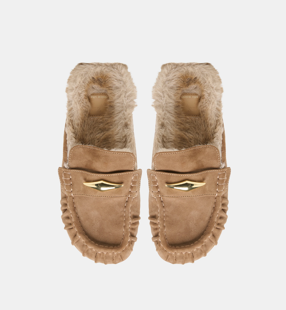 A pair of Dolce Vita Jodero  tan suede moccasin-style flats with fluffy beige faux-fur lining and a gold wing-shaped metal accent on the front, shown against a plain light gray background.