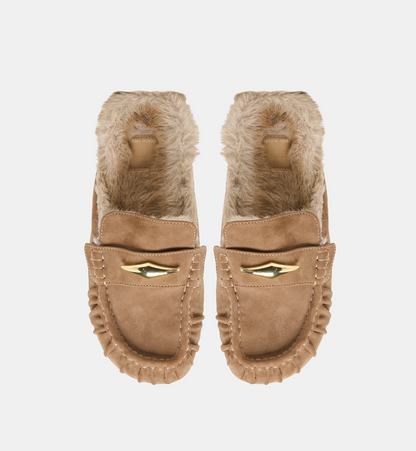 A pair of Dolce Vita Jodero  tan suede moccasin-style flats with fluffy beige faux-fur lining and a gold wing-shaped metal accent on the front, shown against a plain light gray background.